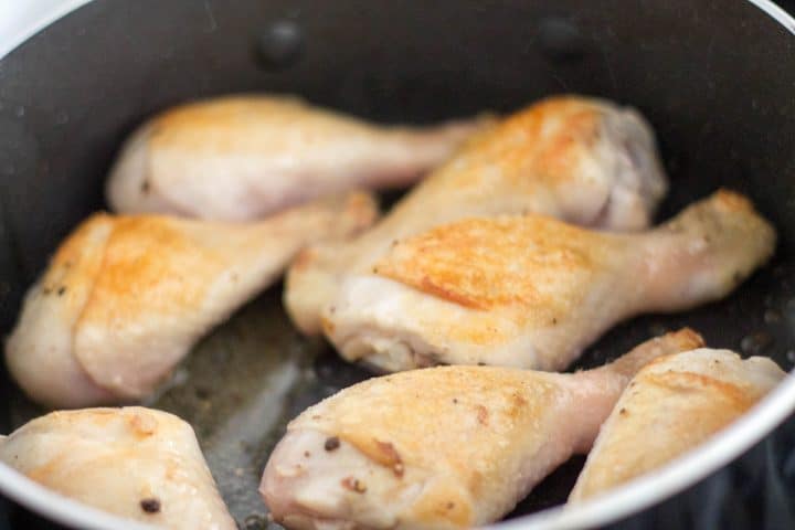 Chicken drumsticks with golden brown skin being seared.