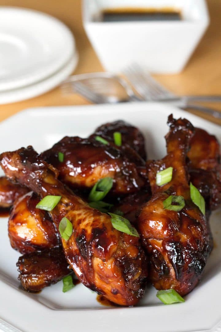 A close up of chicken drumsticks smothered in a sticky brown sauce and garnished with sliced green onions