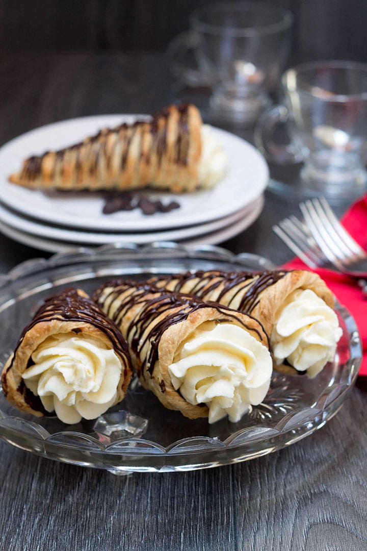 dark chocolate cream horns on a plate ready to serve with forks and a napkin and more plates of pastries in the background