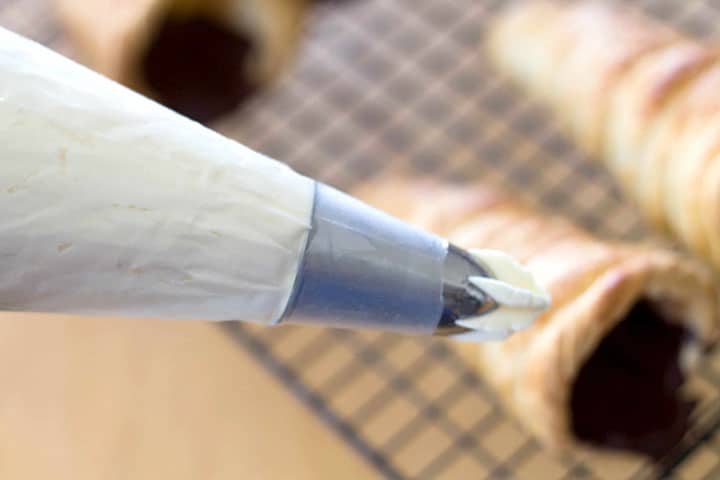 A close up of the top of a piping bag filled with whipped cream with a decorative tip.