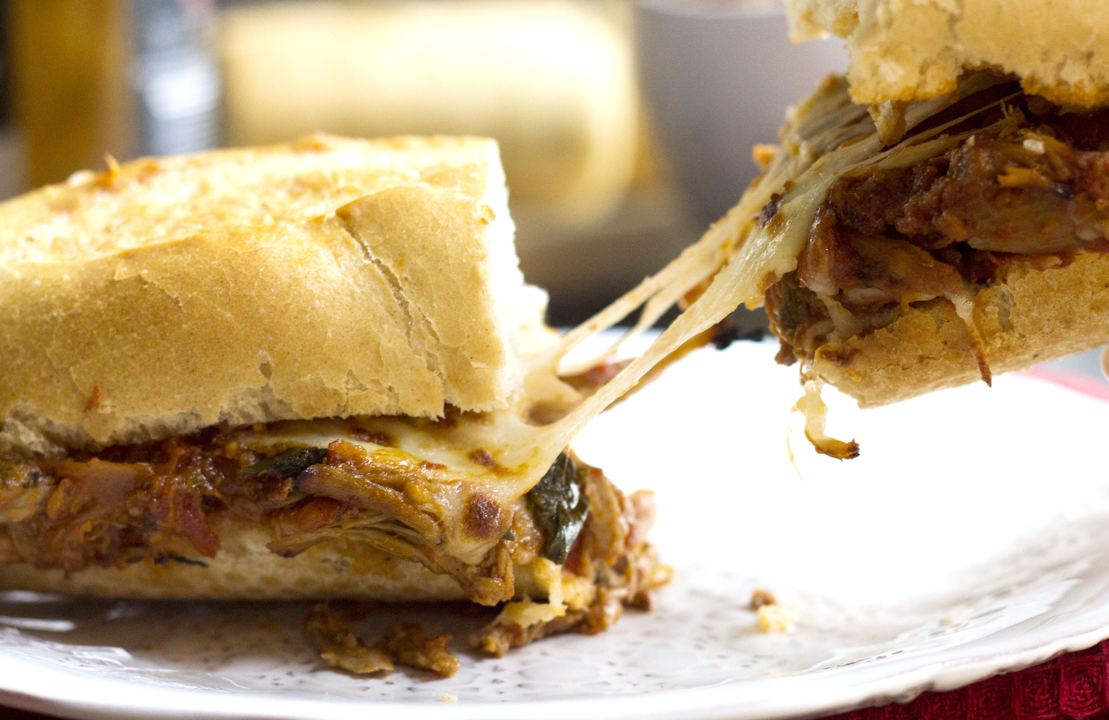 A pulled pork sandwich being pulled apart, with stringy cheese