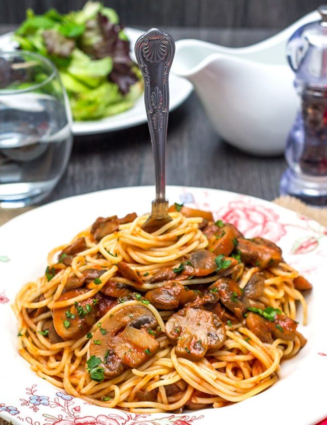 A dish piled high with Spaghetti With Mushroom Tomato Sauce and a fork twirling the pasta