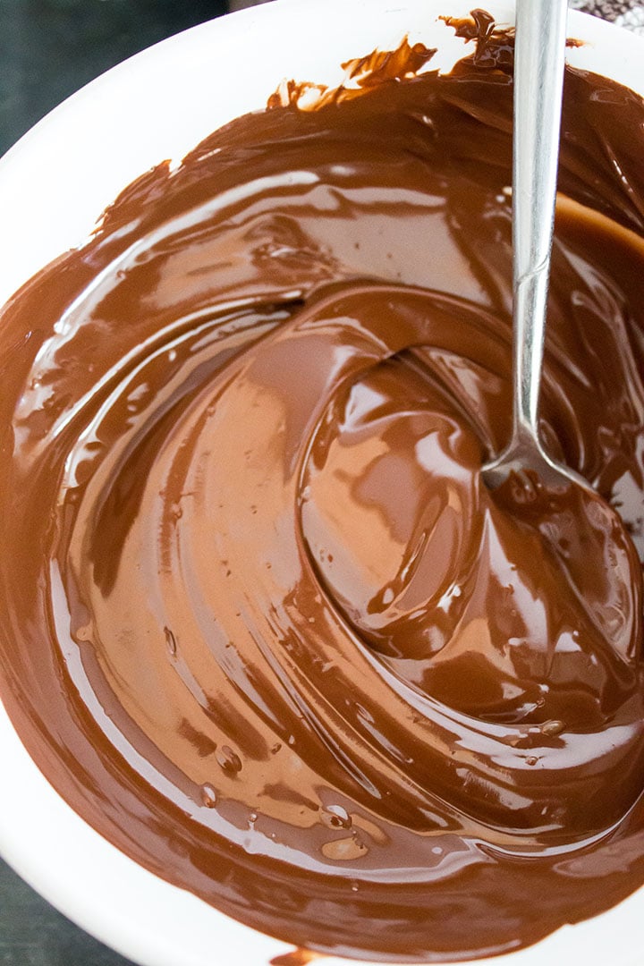 Melted chocolate being stirred by a spoon in a white bowl