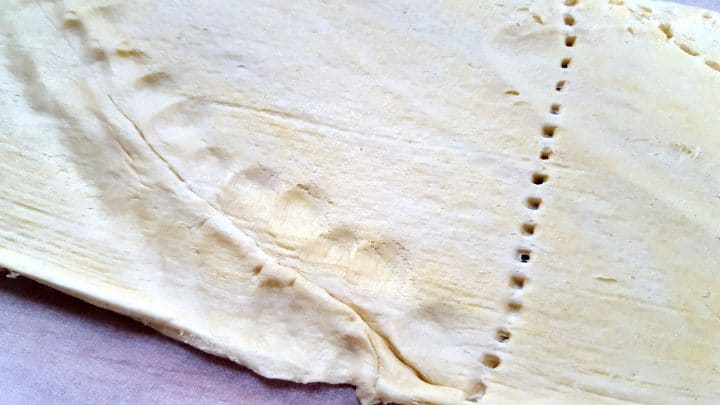 the dough unrolled on a cutting board with the cuts sealed back together