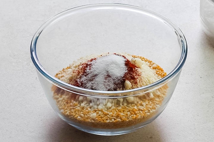 The breadcrumbs in a glass bowl topped with the grated cheese and seasoning