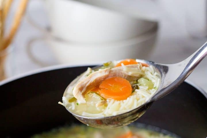 A ladle of Homemade Chicken Noodle Soup over a soup pot