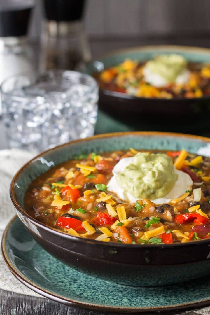 A close up of A bowl of Mexican Rice and Bean soup topped with sour cream and guacamole 