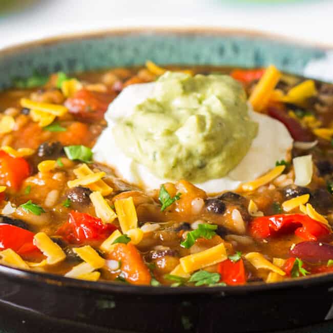a big bowl of Mexican soup topped with cheddar cheese, sour cream and Guacamole