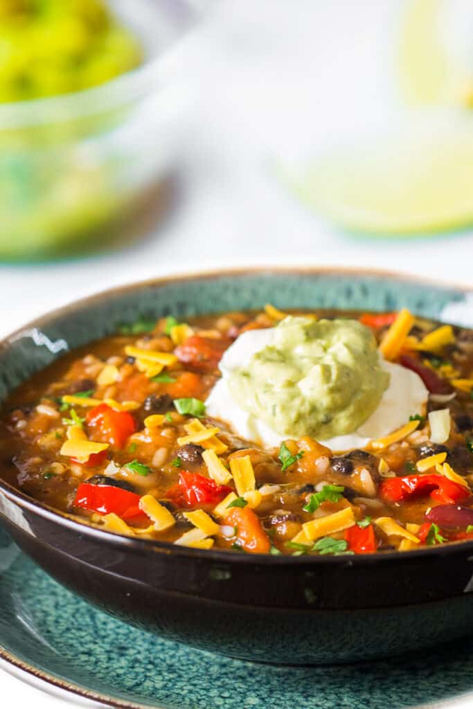 a bowl of Mexican soup with rice and beans topped with Guacamole and sour cream