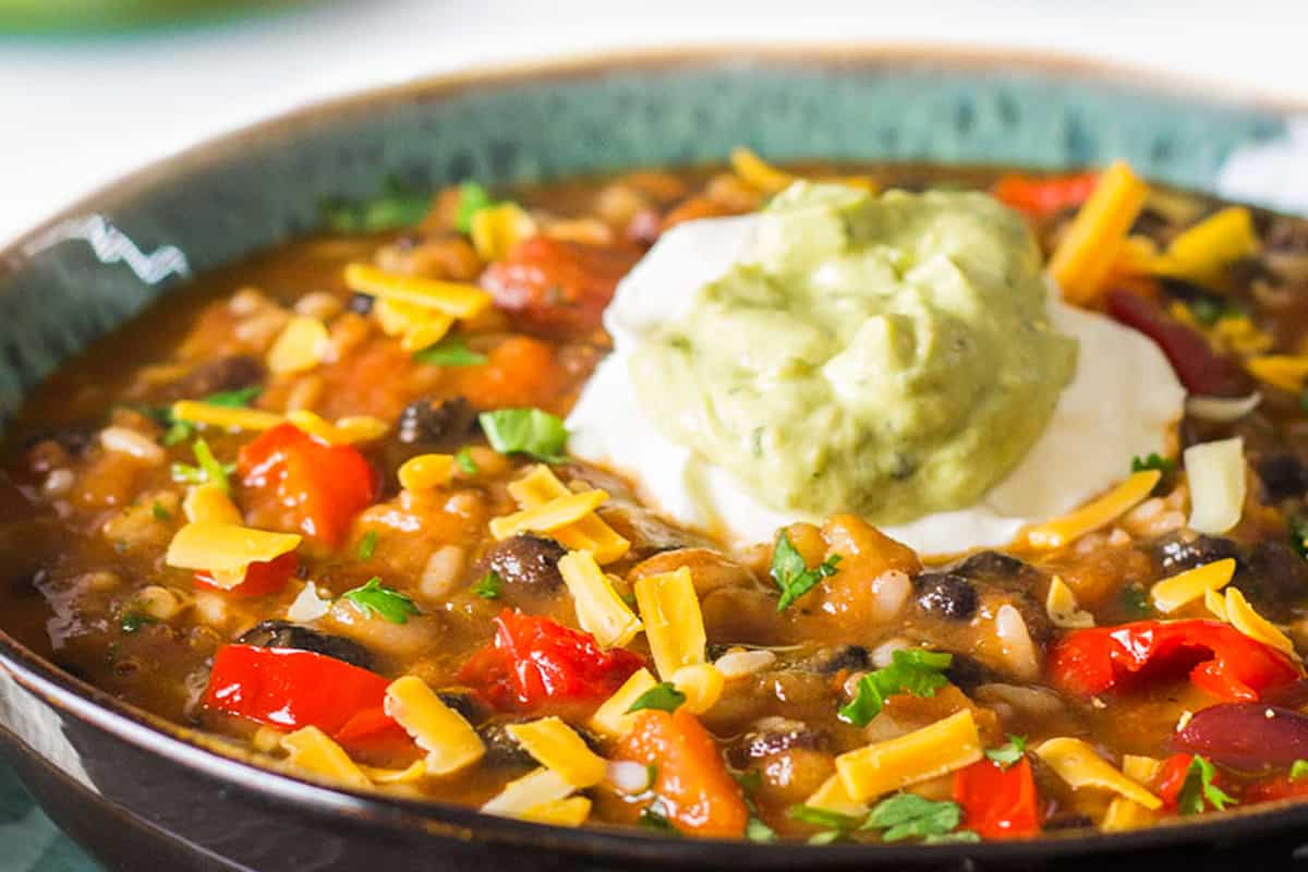 a bowl of Mexican soup topped with Guacamole and sour cream