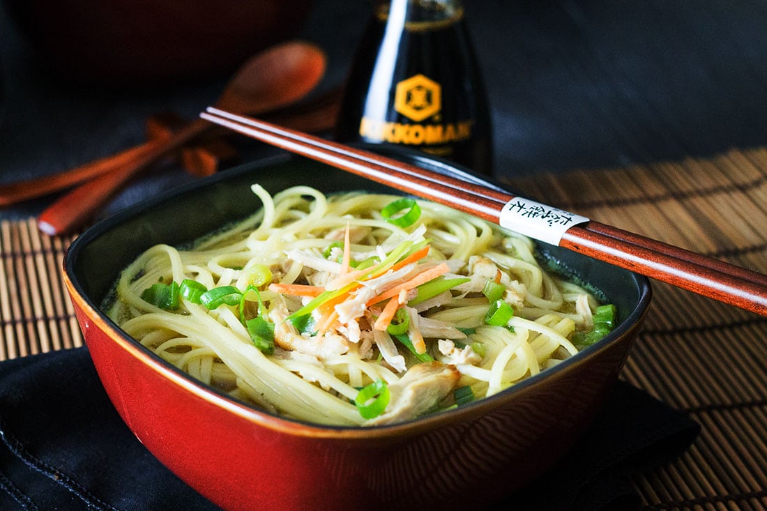 A bowl of noodles with chopsticks and soy sauce in the background