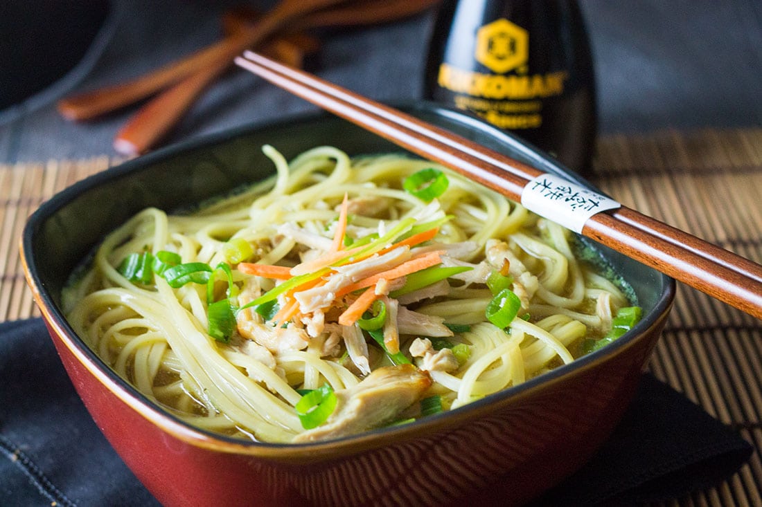 A bowl of chicken noodle soup with chopsticks and soy sauce in the frame