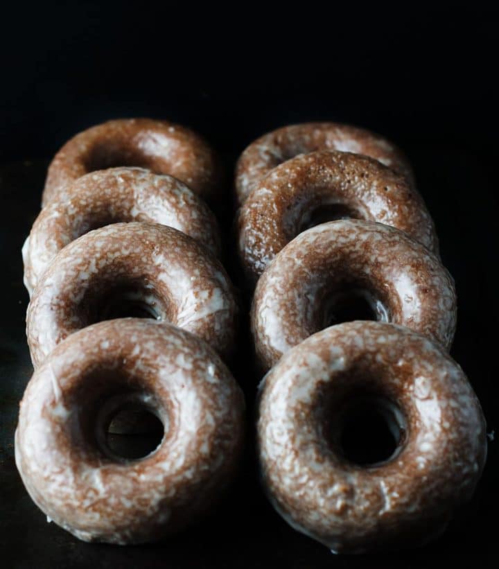 Eight chocolate glazed doughnuts in two rows laying up against each other. 