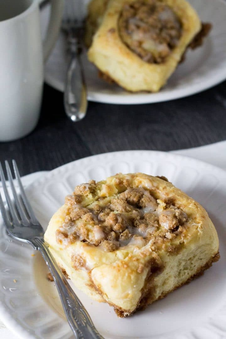 A Cinnamon Crumb Bun on a plate drizzled with icing ready to eat