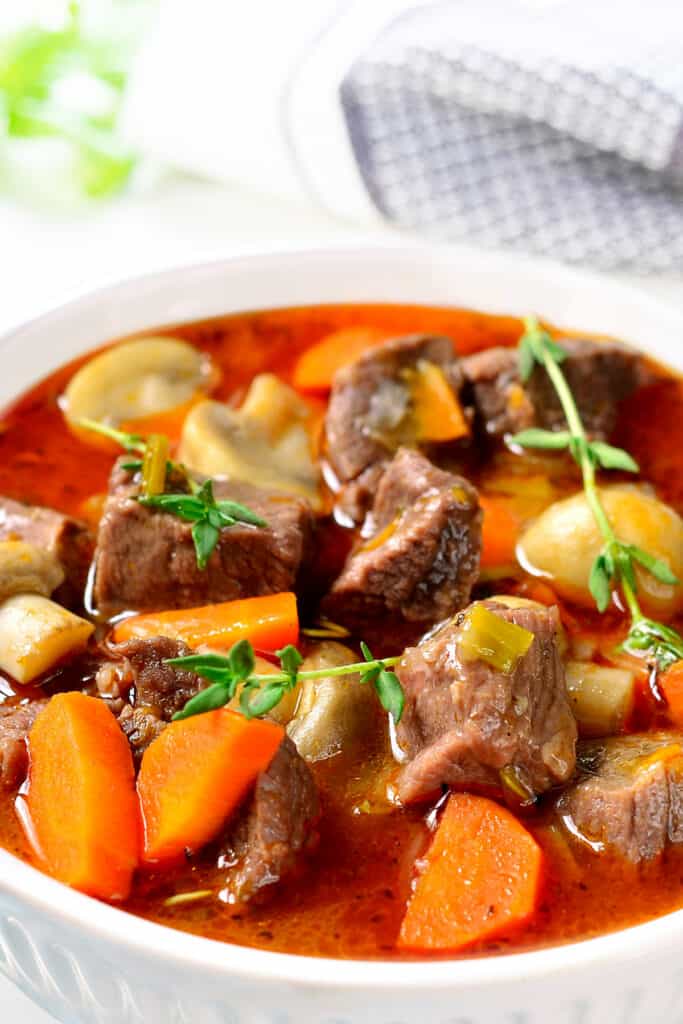 A bowl full of beef stew with carrots and mushrooms