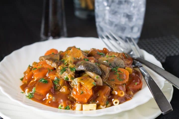 A close up of the Italian Beef Stew served on pasta with salt and pepper on the table in the background