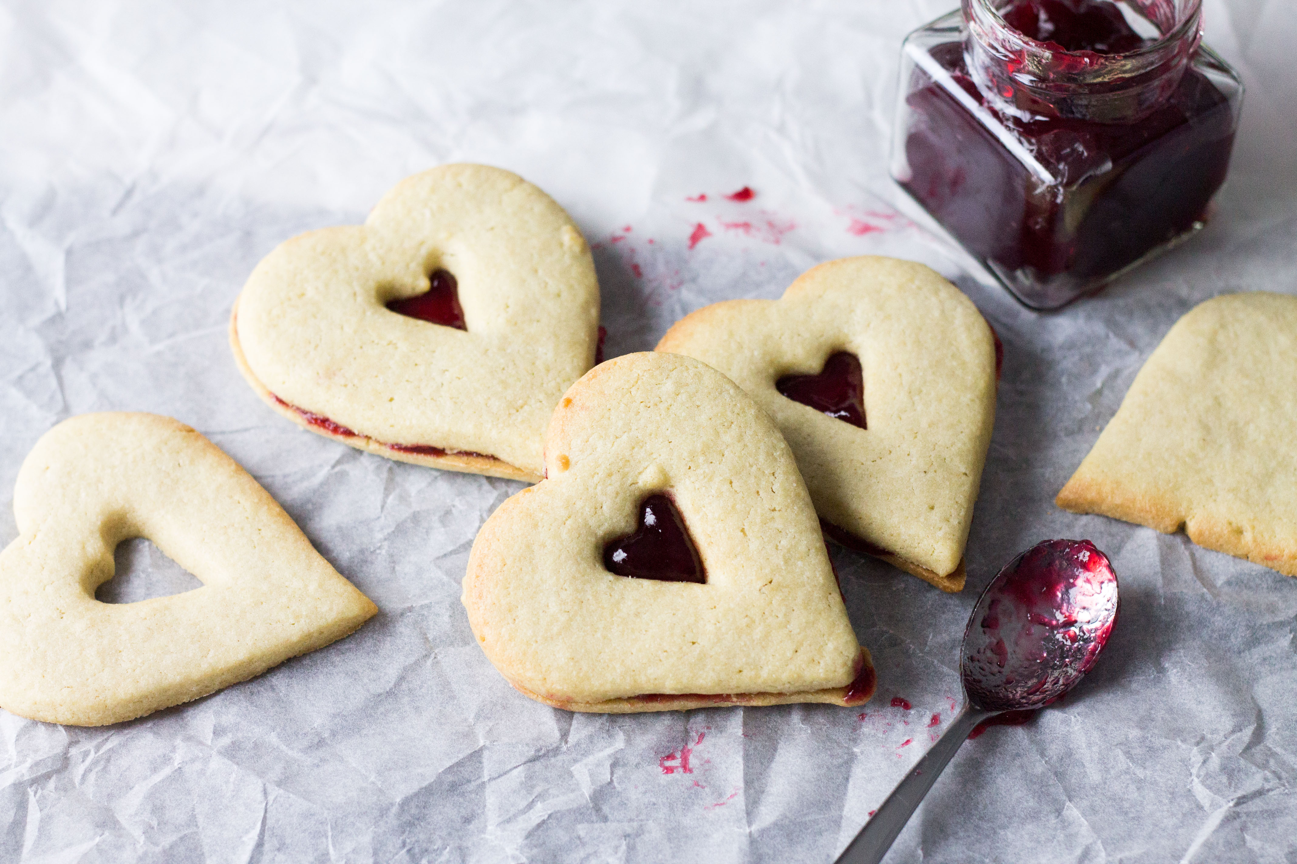A close up of three raspberry butter cookies with raspberry jam in the background 