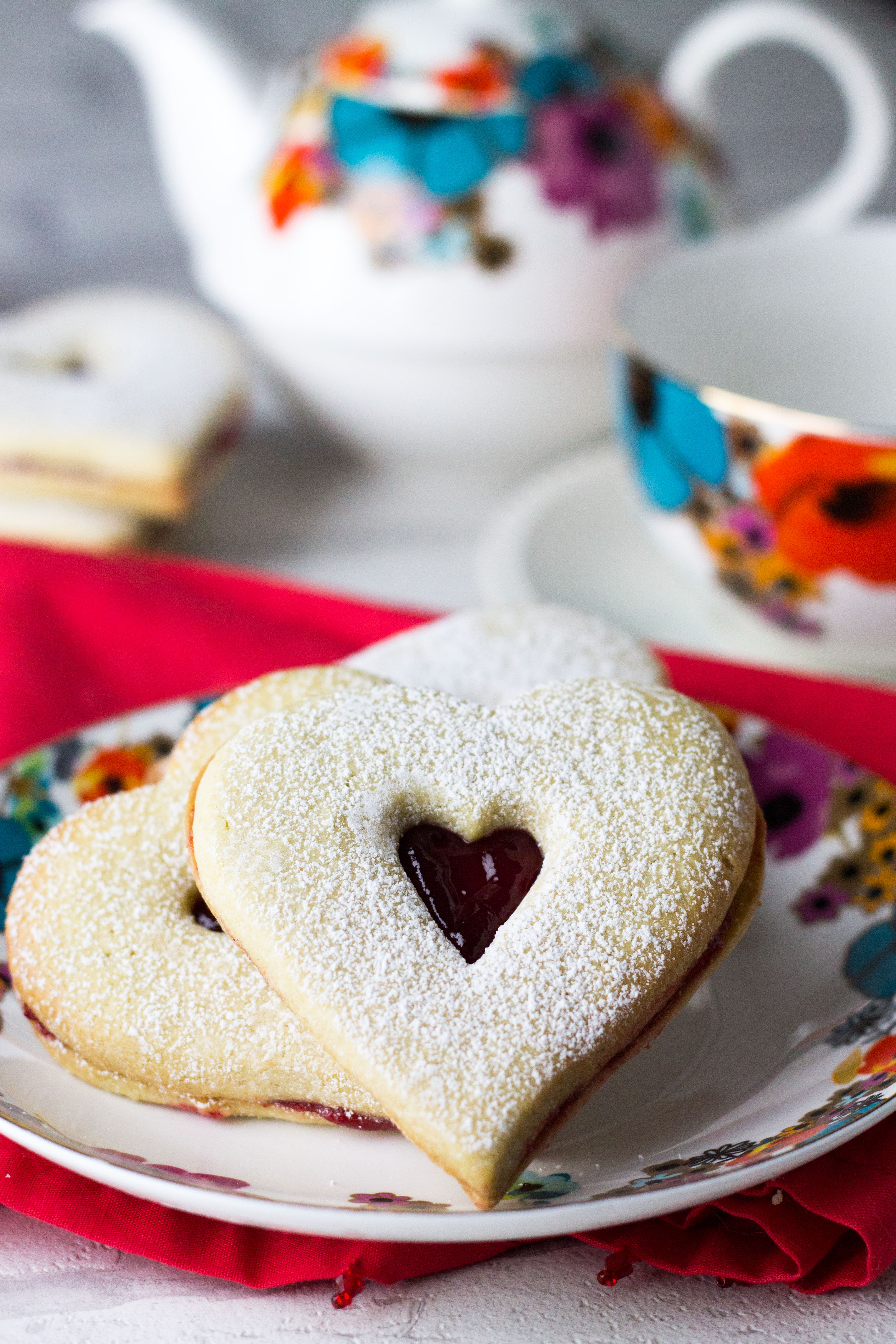 A close up of raspberry butter cookies with a tea service in the background