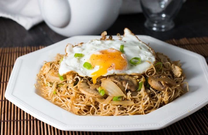 Stir fried rice noodles with vegetables topped with a fried egg with the yolk dripping into the noodles