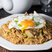 A plate of noodles with a fried egg on top and chopped green onions