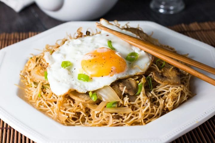 a close up of the Fried Eggs with Chinese Noodles with chopsticks on the plate and garnished with sliced green onions.