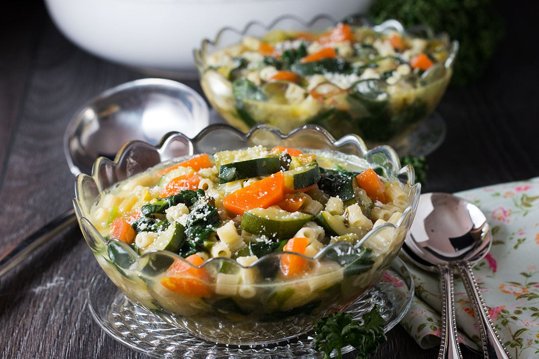 Two bowls of Spring Vegetable Soup in clear glass bowls with serving spoons