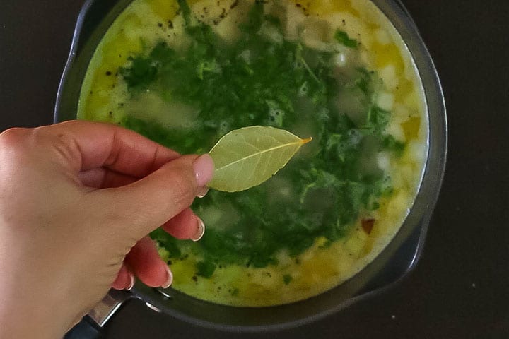 A bay leaf being dropped in the pot with the parsley, stock and rice mixture