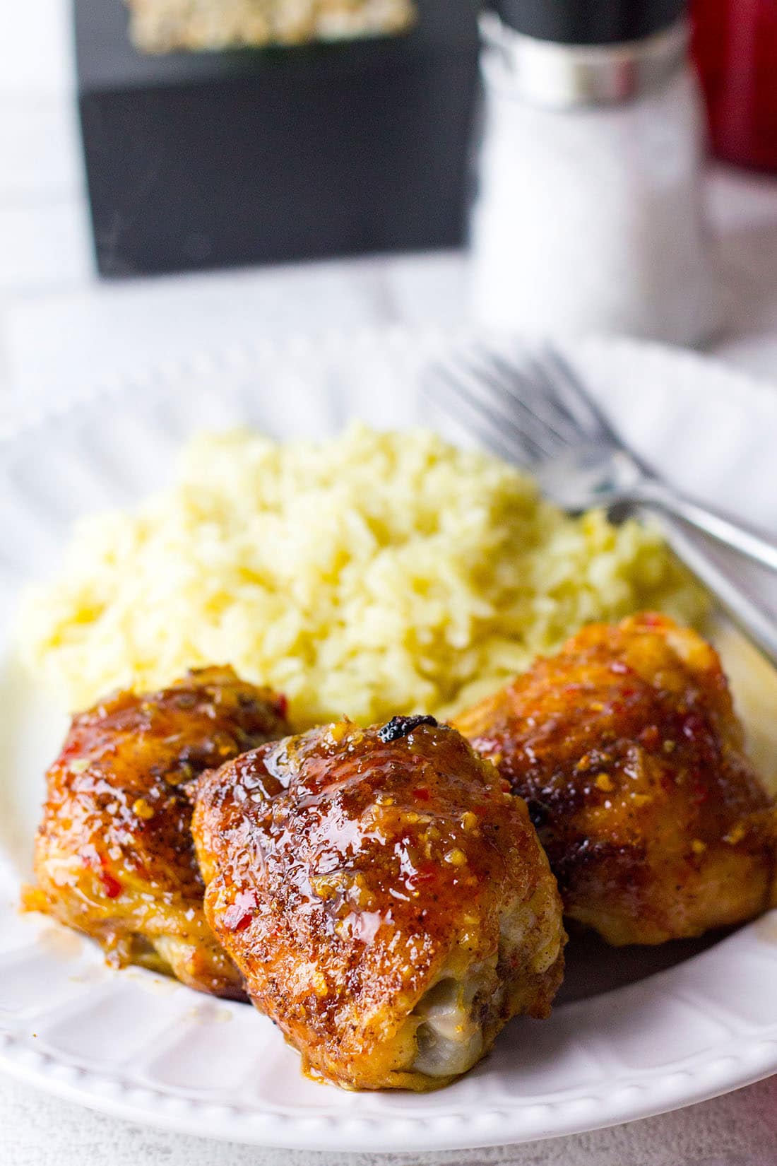 The chicken with it's sticky sauce on the plate with yellow rice and two forks.