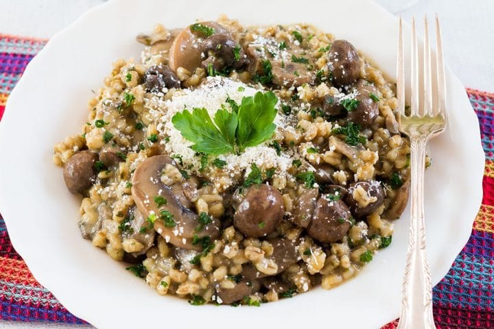 A close up of Skinny Mushroom & Barley Risotto topped with parsley and grated cheese and a fork laying next to it