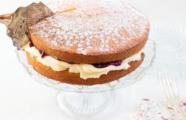 Victoria sponge cake on a cake stand with a cake slice, slicing through