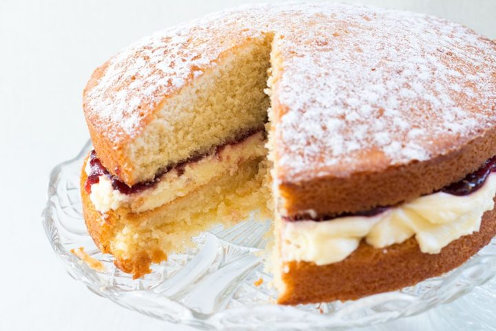 Classic Victoria Sponge Cake with a piece missing on a glass cake stand