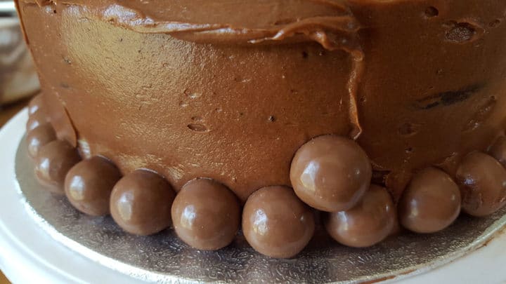 A close up of a chocolate cake on a plate, with chocolate malt balls