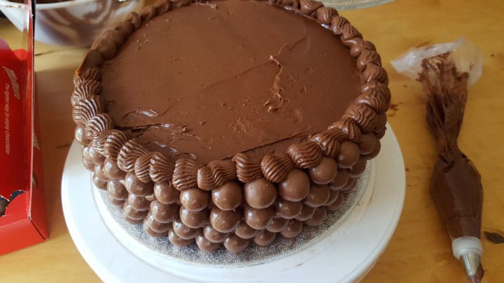 A chocolate cake on a plate process shot of icing and malt ball decoration