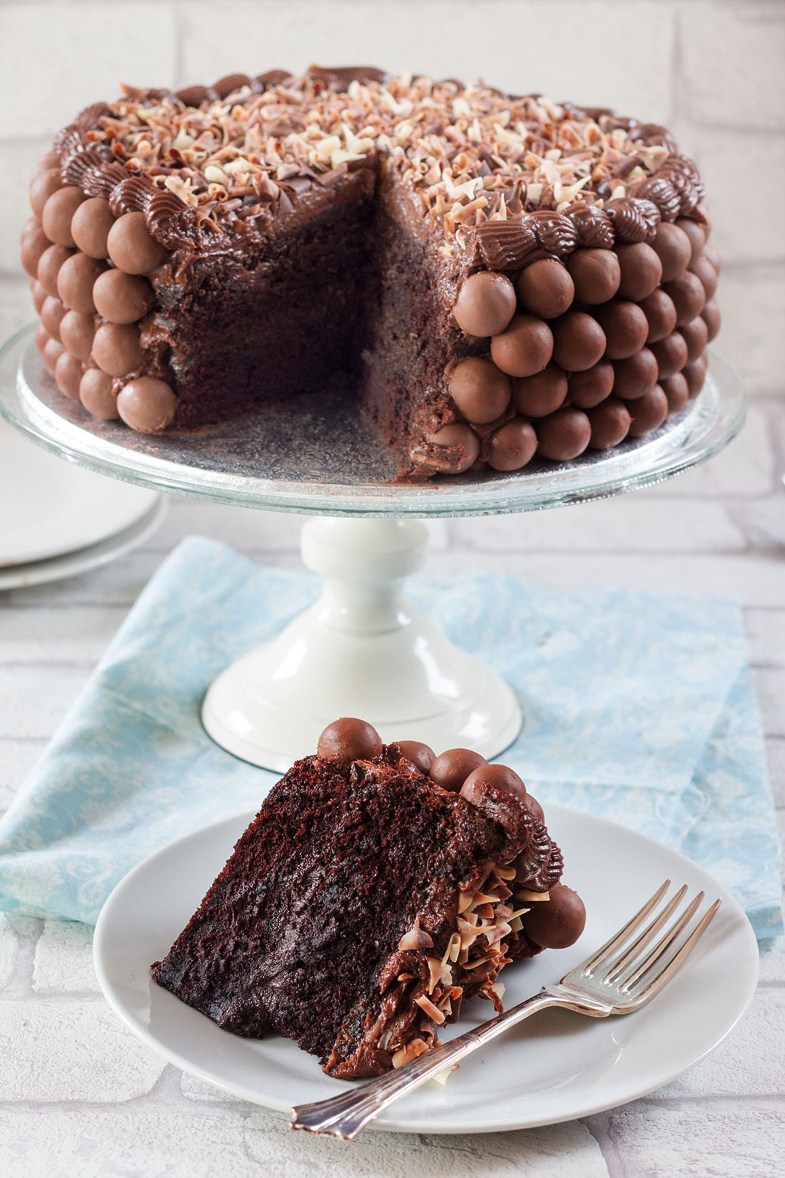 A piece of chocolate cake on a plate, with Chocolate cake on serving plate in the background