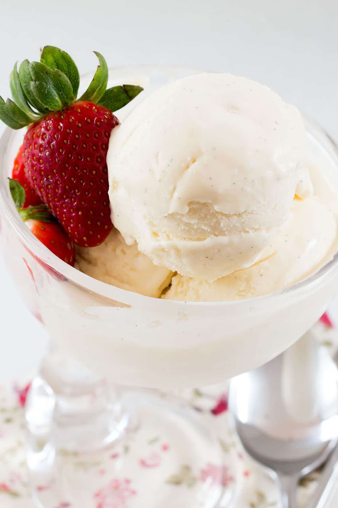 A glass bowl filled scoops of vanilla ice cream garnished with a strawberry