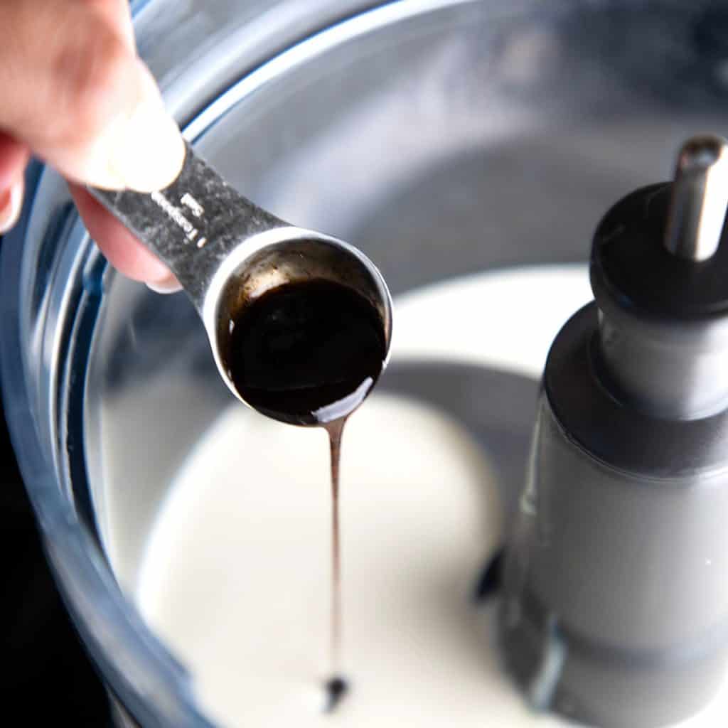 vanilla bean paste being added to cream and condensed milk in a bowl