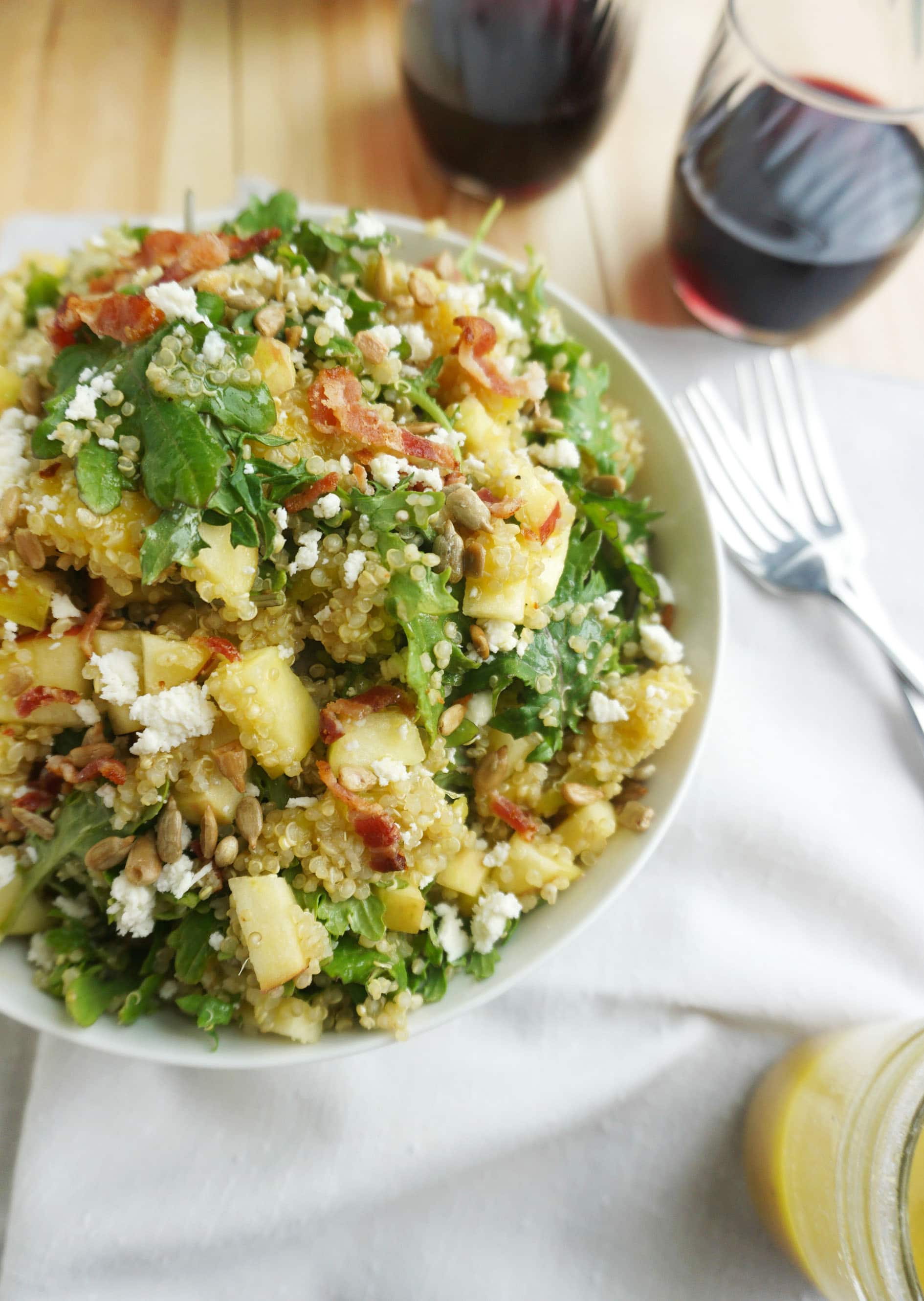Bacon Quinoa Salad with Lemon Dijon Dressing in a bowl with forks and two glasses of red wine