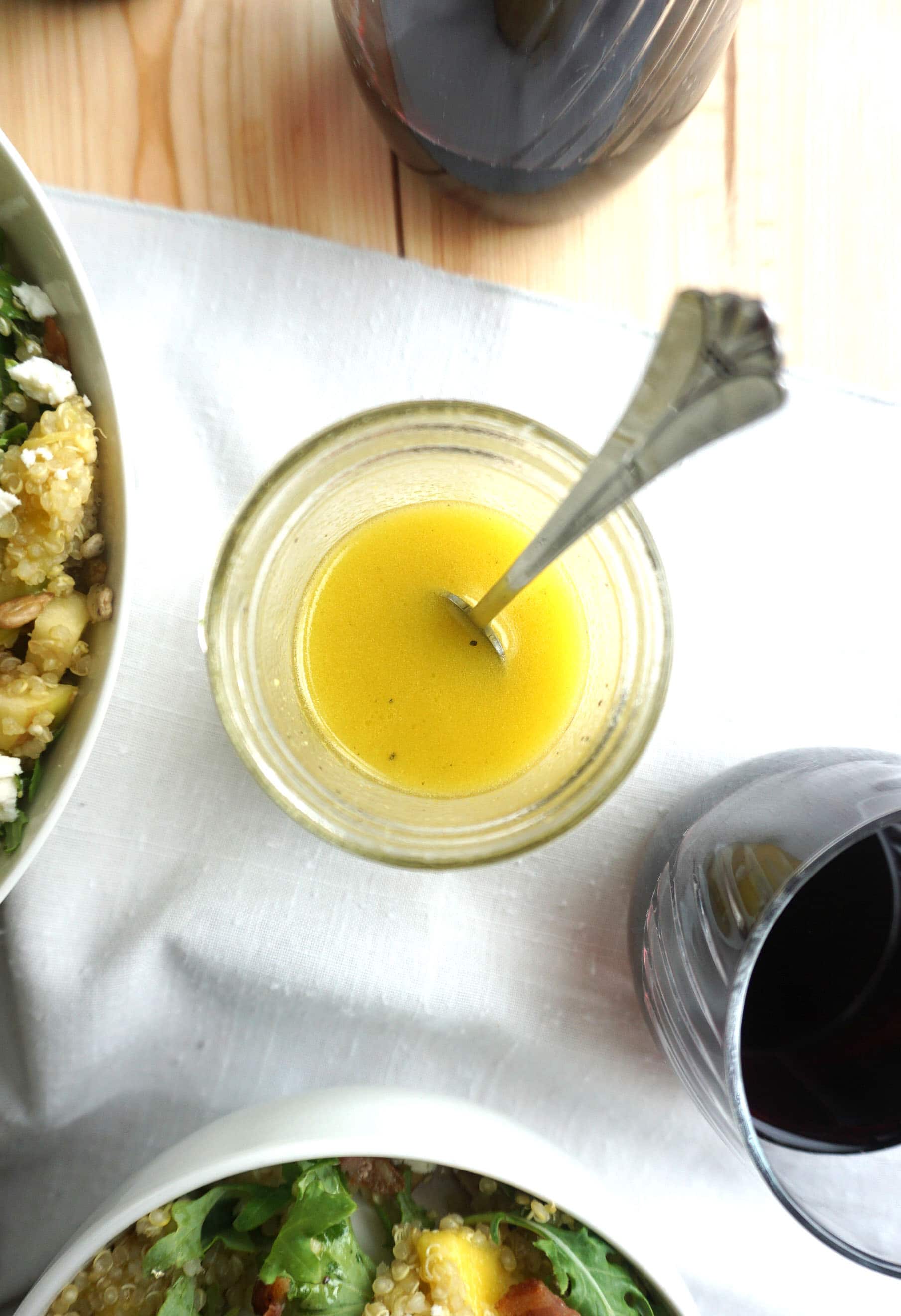arial view of dijon mustard in a pot with a spoon and the edge of a salad bowl and glass of red wine