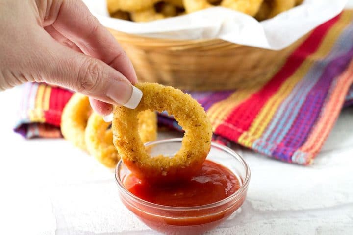 A Skinny Seasoned Baked Onion Ring being dipped into a little bowl of ketchup 