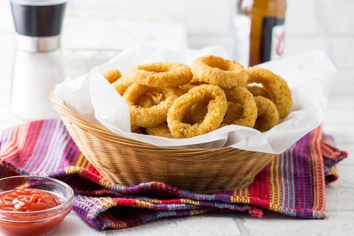 A basket on baked onion rings with a salt shaker in the background