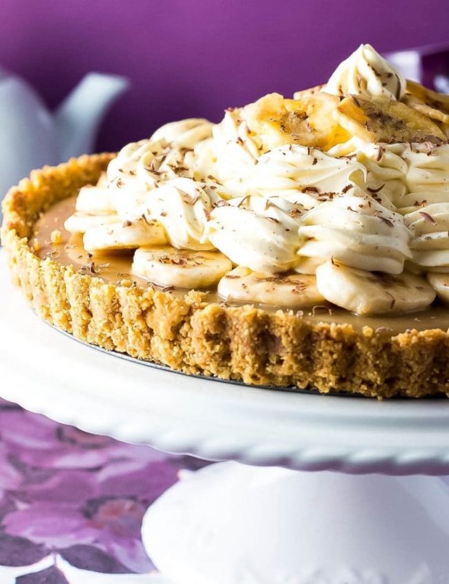 The Banoffee Pie on a cake stand showing the crust, caramel layer, banana layer, whipped cream and banana chips as decoration