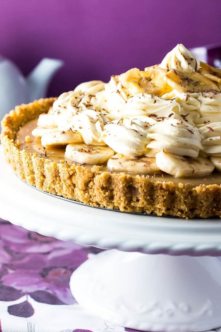 The Banoffee Pie on a cake stand showing the crust, caramel layer, banana layer, whipped cream and banana chips as decoration