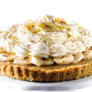 The Banoffee Pie on a cake stand showing the crust, caramel layer, banana layer, whipped cream and banana chips as decoration