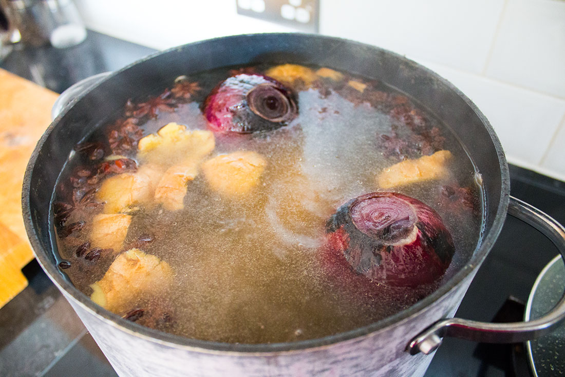 oxtail, whole roasted red onions, ginger boiling in a large pan