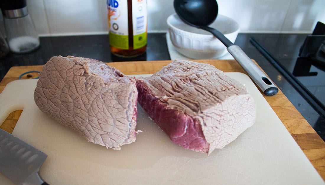 rare cooked beef joint cut in half on a white chopping board