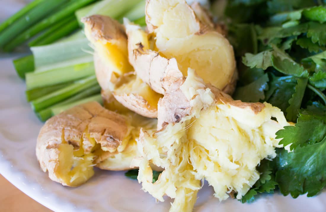 a white plate with crushed ginger root, chopped spring onions and herbs