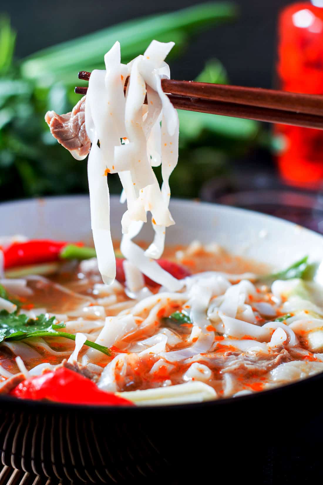 rice noodles on chop sticks over a bowl of Beef Noodle Pho