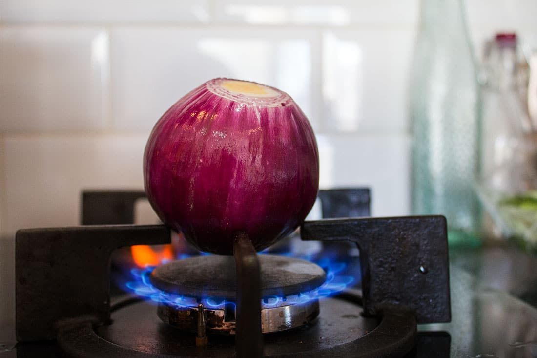 a whole peeled red onion roasting on a gas ring