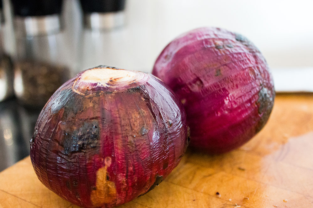 two freshly roasted red onions on a wooden cutting board