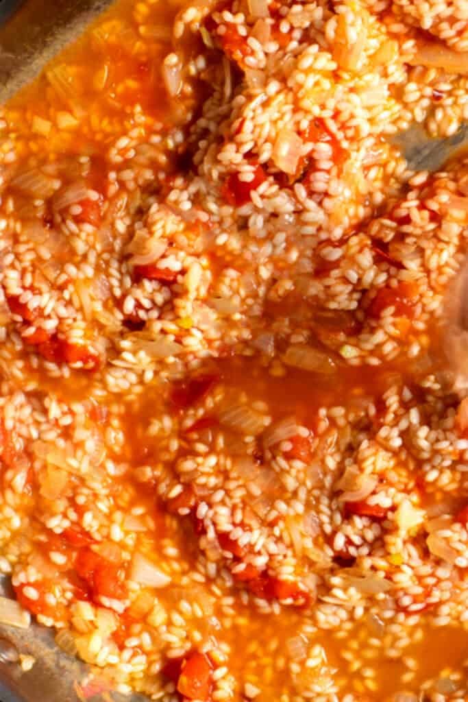 risotto is cooked in a pan with the stock and tomatoes